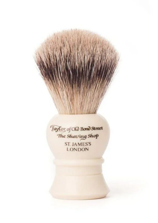 A small ivory shaving brush with super badger bristles, presented in a black cylindrical container with a base and brush visible at the top. The container has the inscription 'Taylor of Old Bond Street, London'.